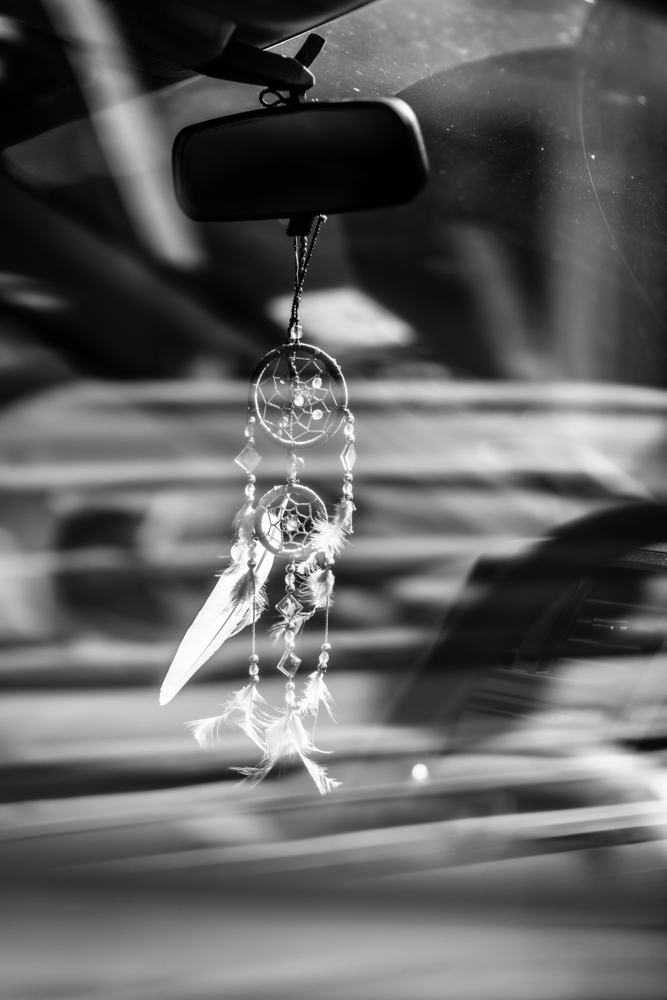 Dreamcatcher hanging from a car mirror black and white dashboard street series