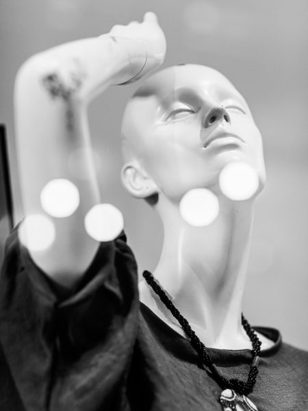 Shop mannequin with her arm lifted and hand above her head dressed in a short sleeve blouse and wearing a necklace