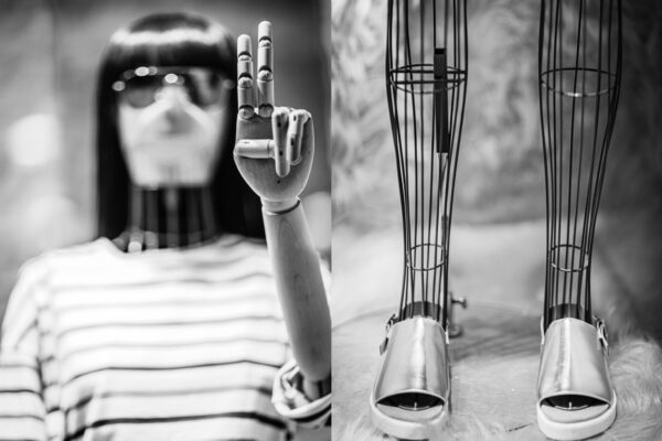 Wooden shop mannequin wearing large circular sunglasses posed with the peace sign and mannequin wire frame legs modelling silver shiny sandals