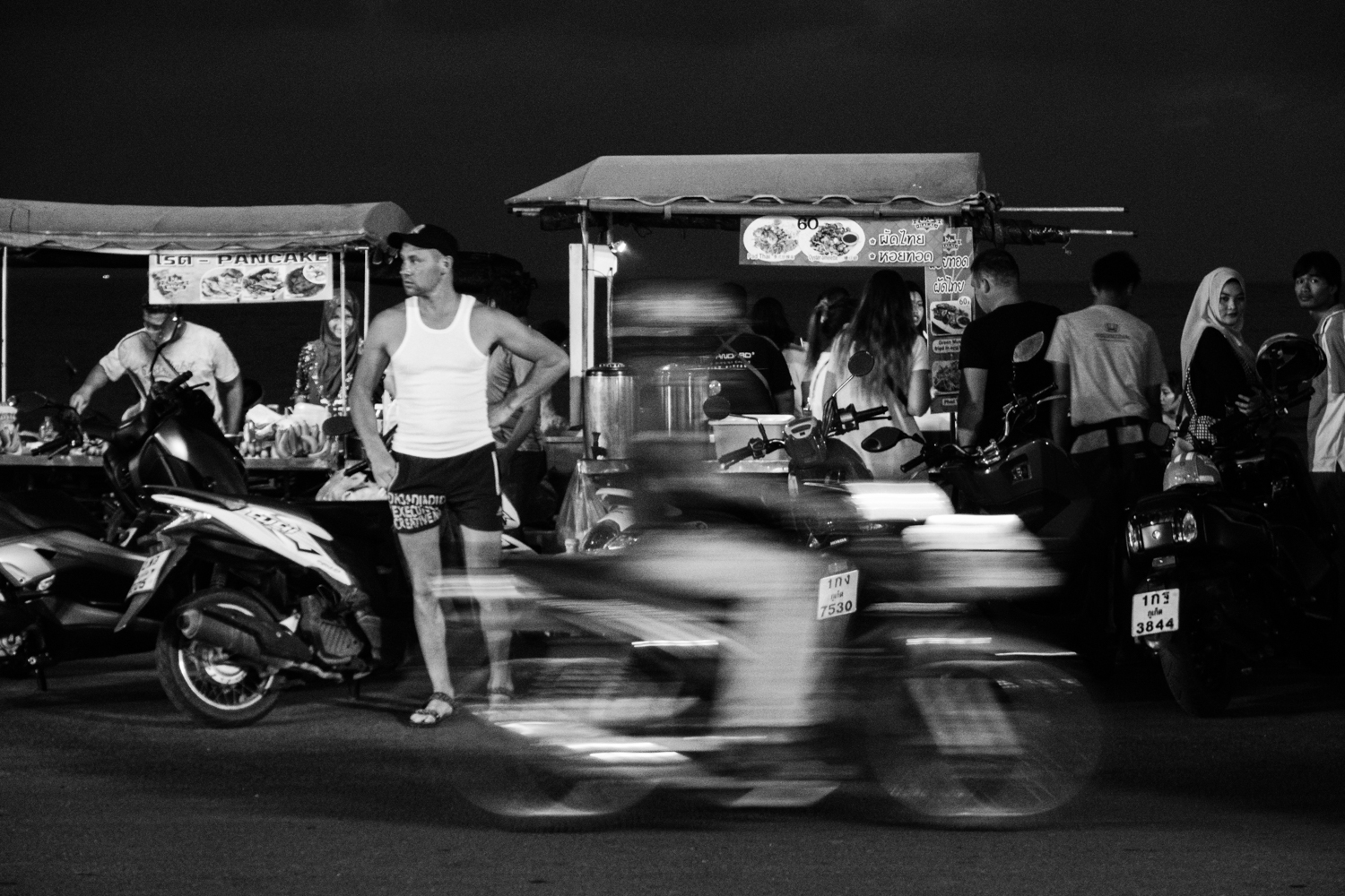 Man trying to cross the road with motorbikes rushing past in a blur along Kalim Beach - Phuket