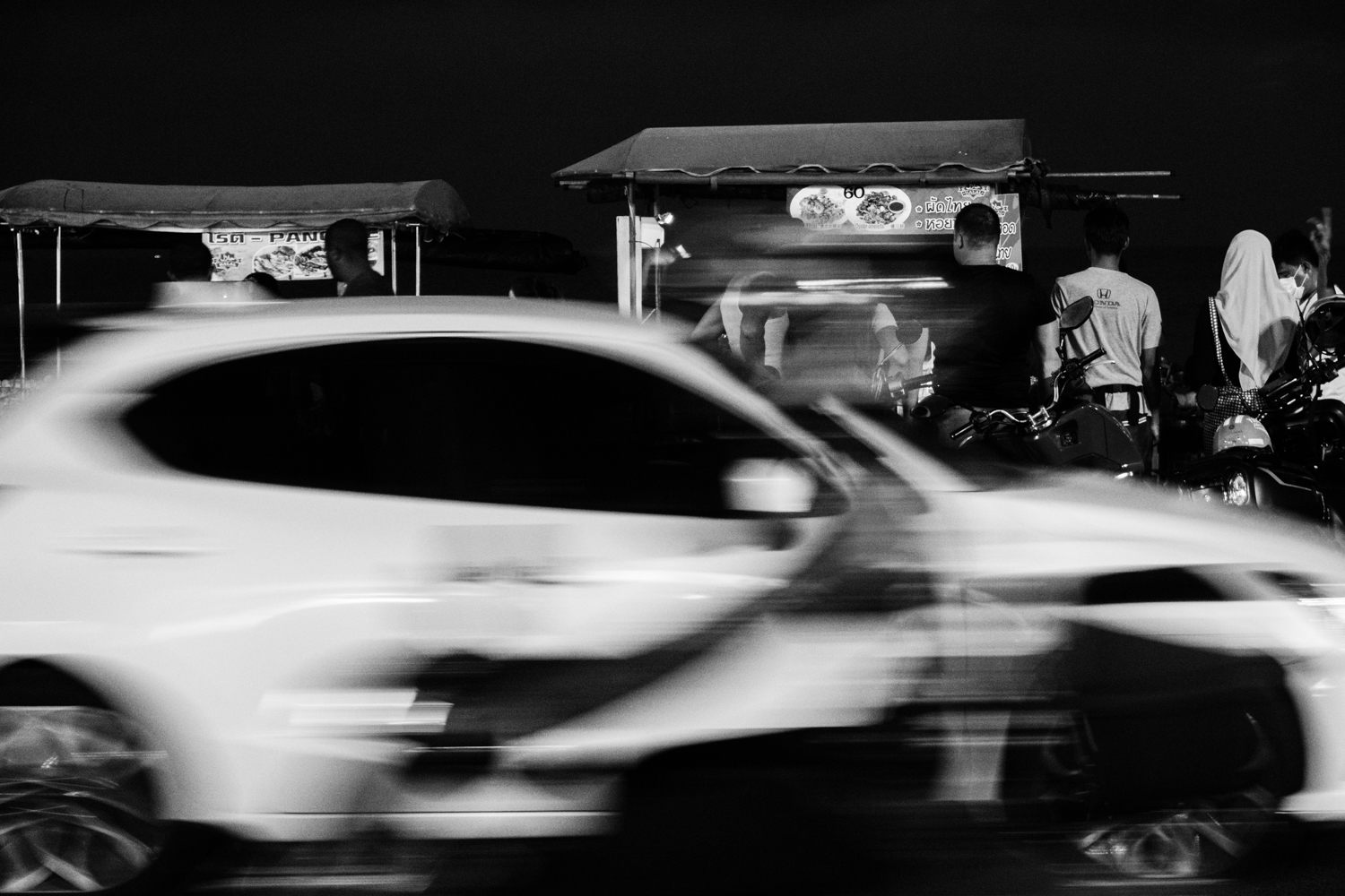 Car rushing past street people waiting for their street food orders along Kalim Beach Phuket Thailand