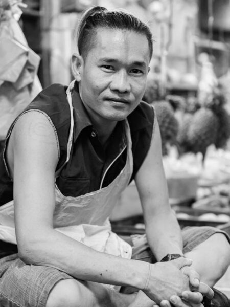 Portrait man sitting in fresh market Chinatown amongst the pineapples