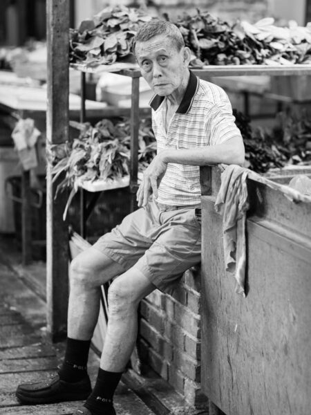 Portrait man sitting amongst vegetables in fresh market chinatown