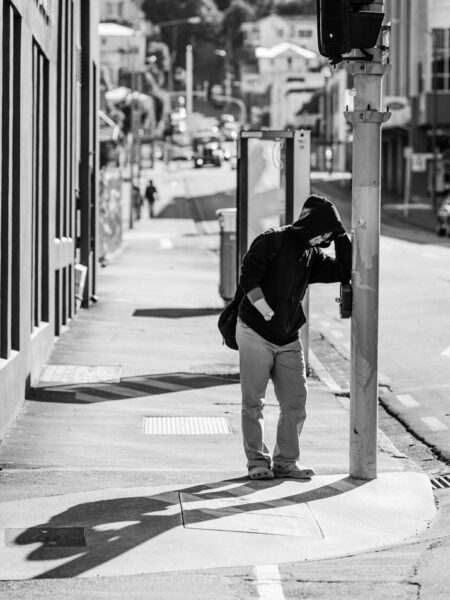 Man standing at a pedestrian crossing leaning against the traffic light. Black and white street photo Wellington - New Zealand