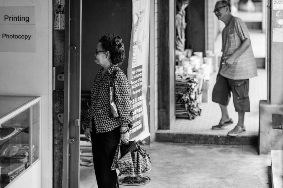 Women wearing a patterned blouse, and holding an umbrella, man onlooking laughing - Pasar Seni, Kuala Lumpur – Malaysia