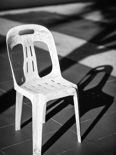 Lone plastic white chair a security guard used to rest on. Black and white street photograph.