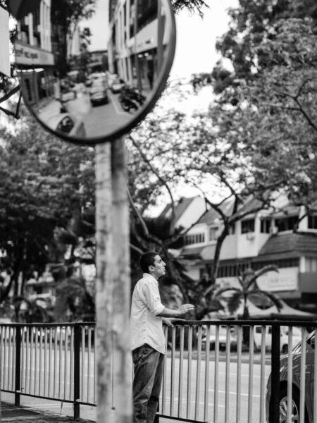 Man standing on the footpath and tapping a rhythm on a metal railing in TTDI - Kuala Lumpur. Street portrait in black and white.