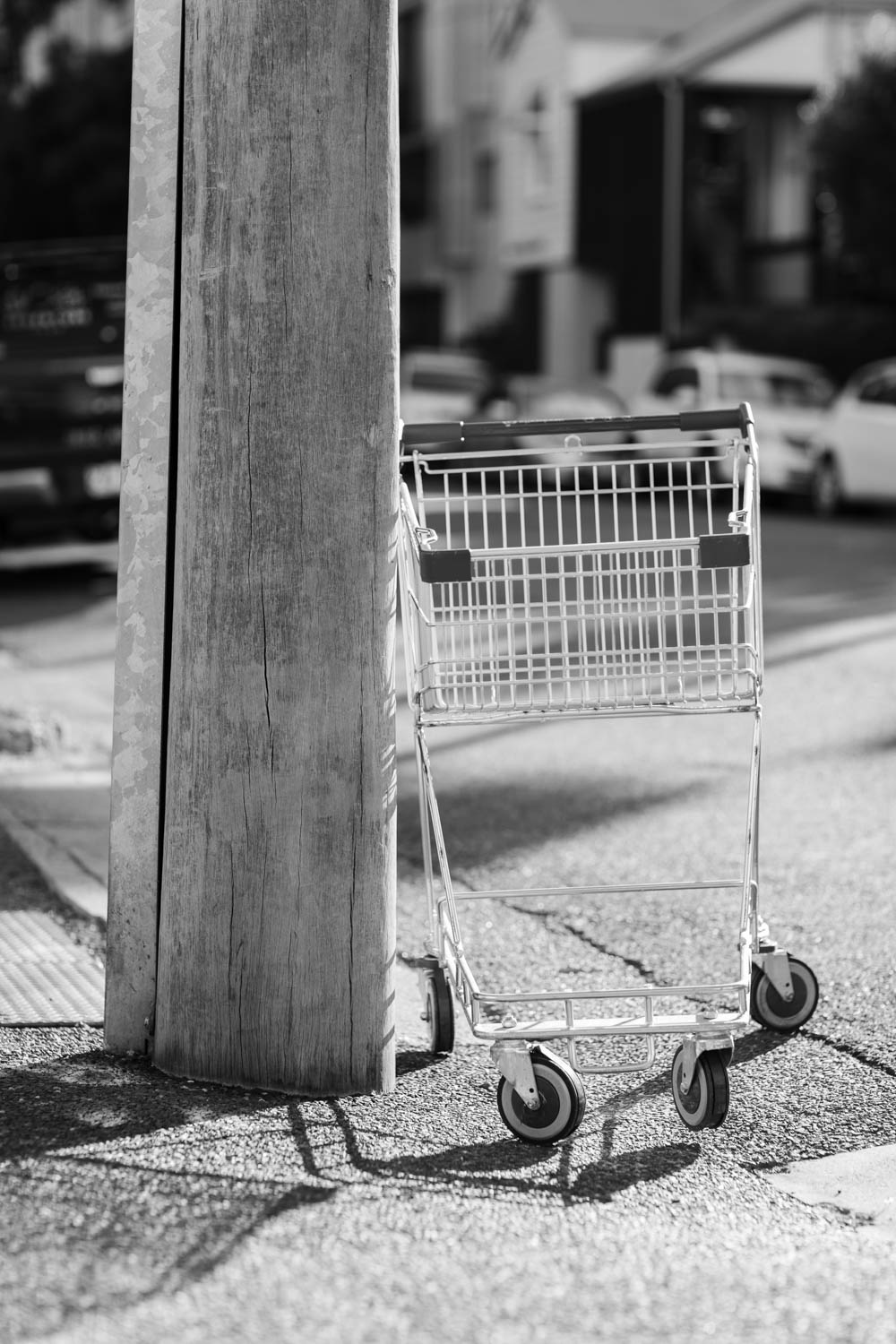 Abandoned supermarket shopping trolley perching against a power pole.