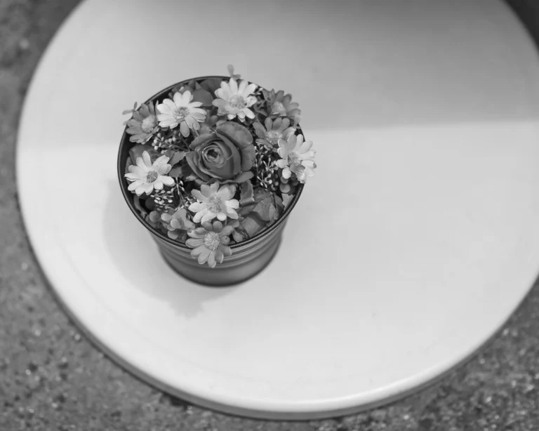 Artificial flowers in a tin bucket sitting on a round table.