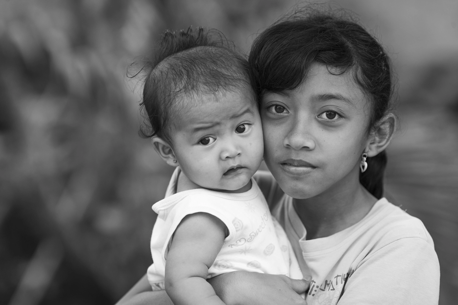 A young girl holding her baby sister in Jimbaran, Bali, Indonesia.