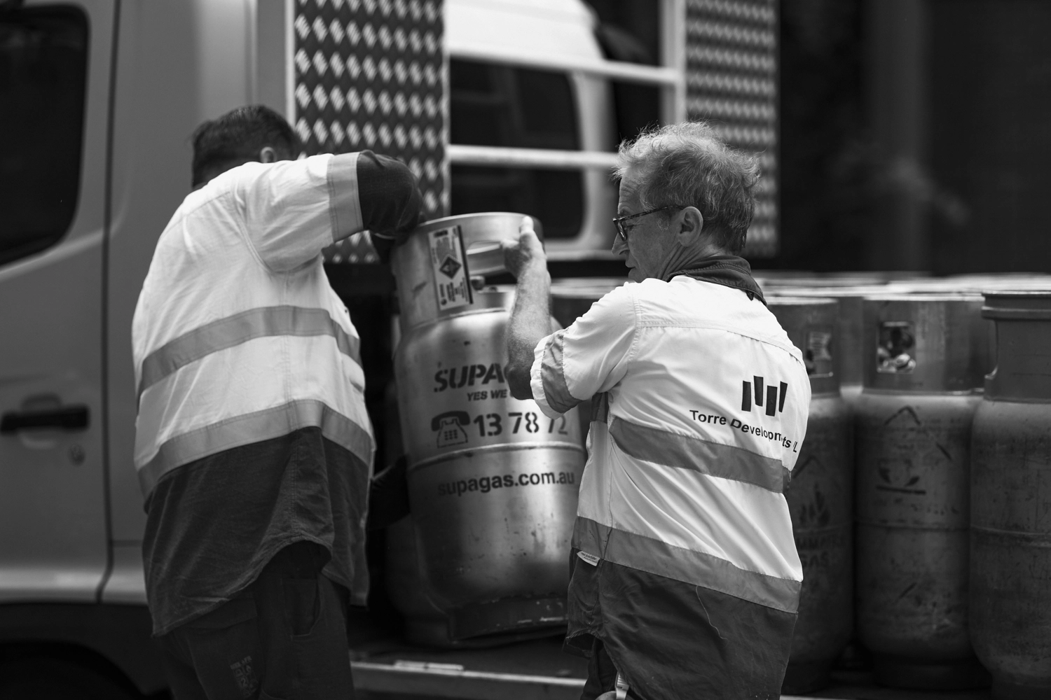 Two men are lifting a Supagas gas bottle onto a truck.