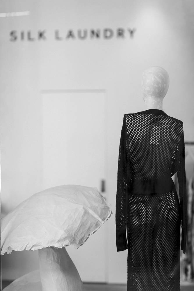 The model is wearing a black mesh long-sleeved top and matching trousers.