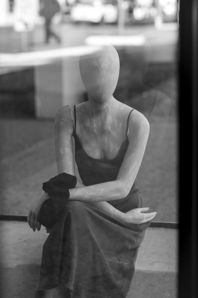 A seated shop mannequin with a reflected street scene in the background.