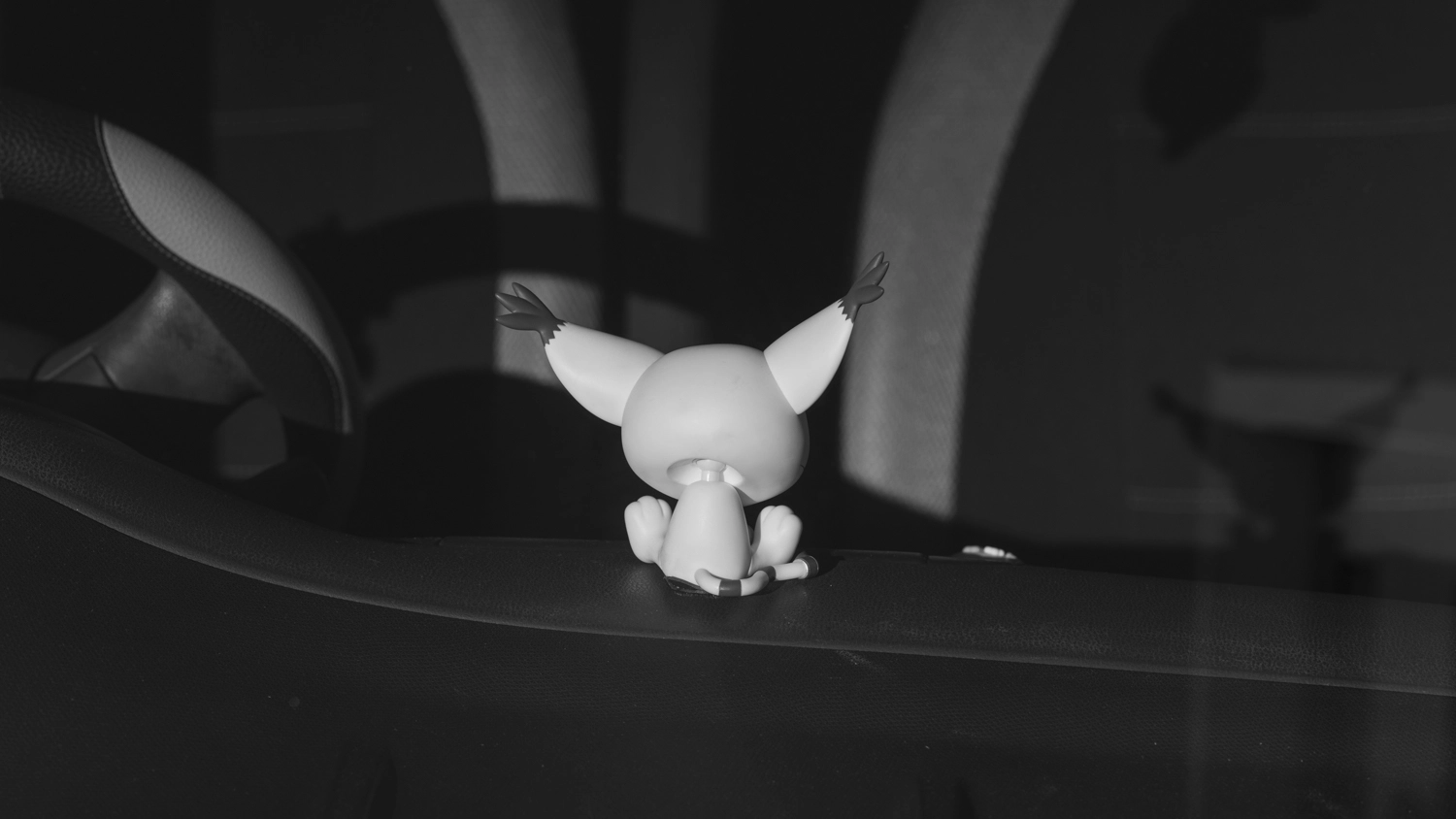 Pikachu figurine on a car dashboard, photographed in shadow and light, Newstead black and white street photo.